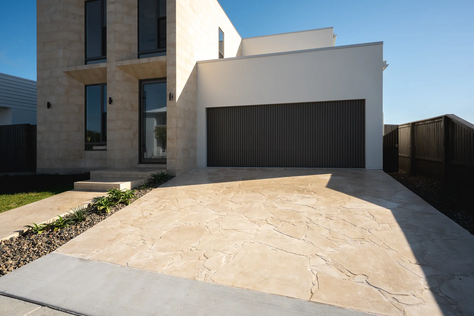 Travertine crazy paving across a driveway to a limestone entrance in afternoon light