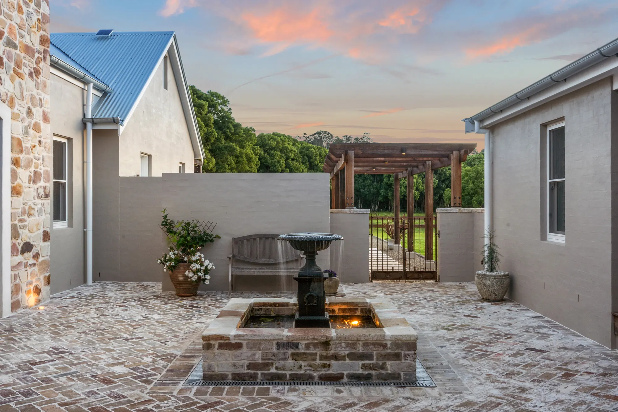 A reclaimed brick courtyard at dusk with the fountain lit from below