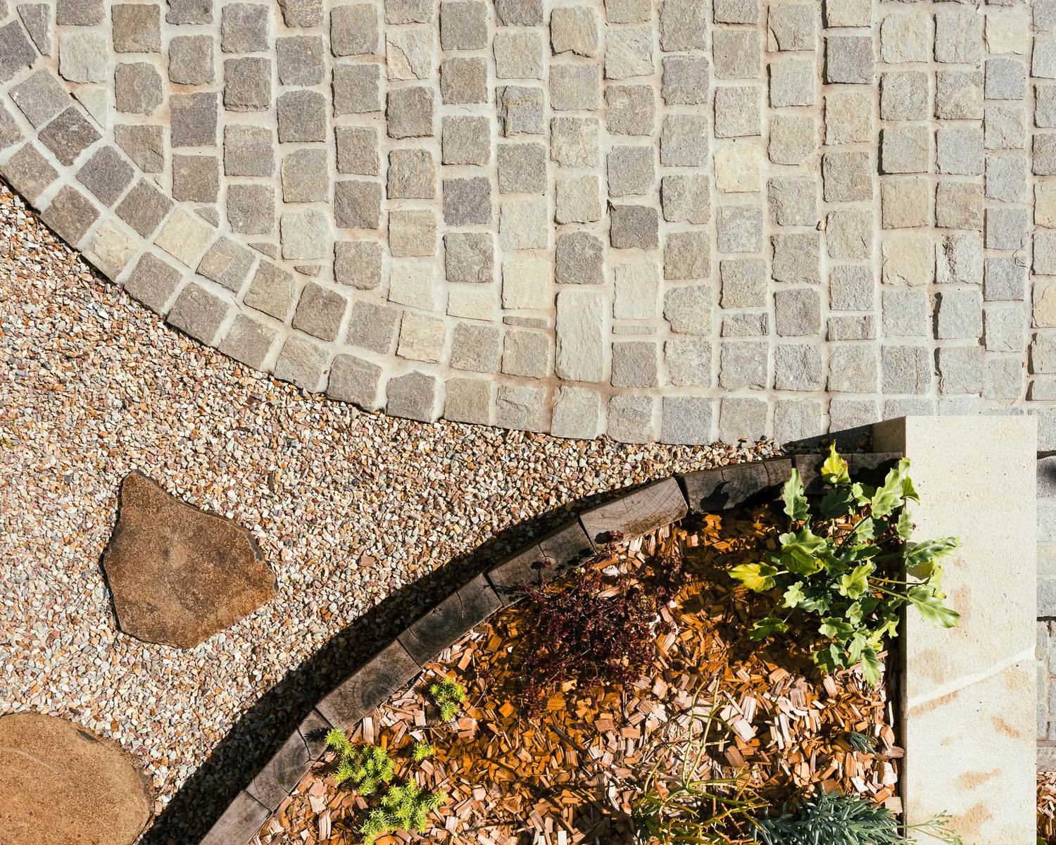 A curve of granite setts meeting exposed aggregate and a sandstone step