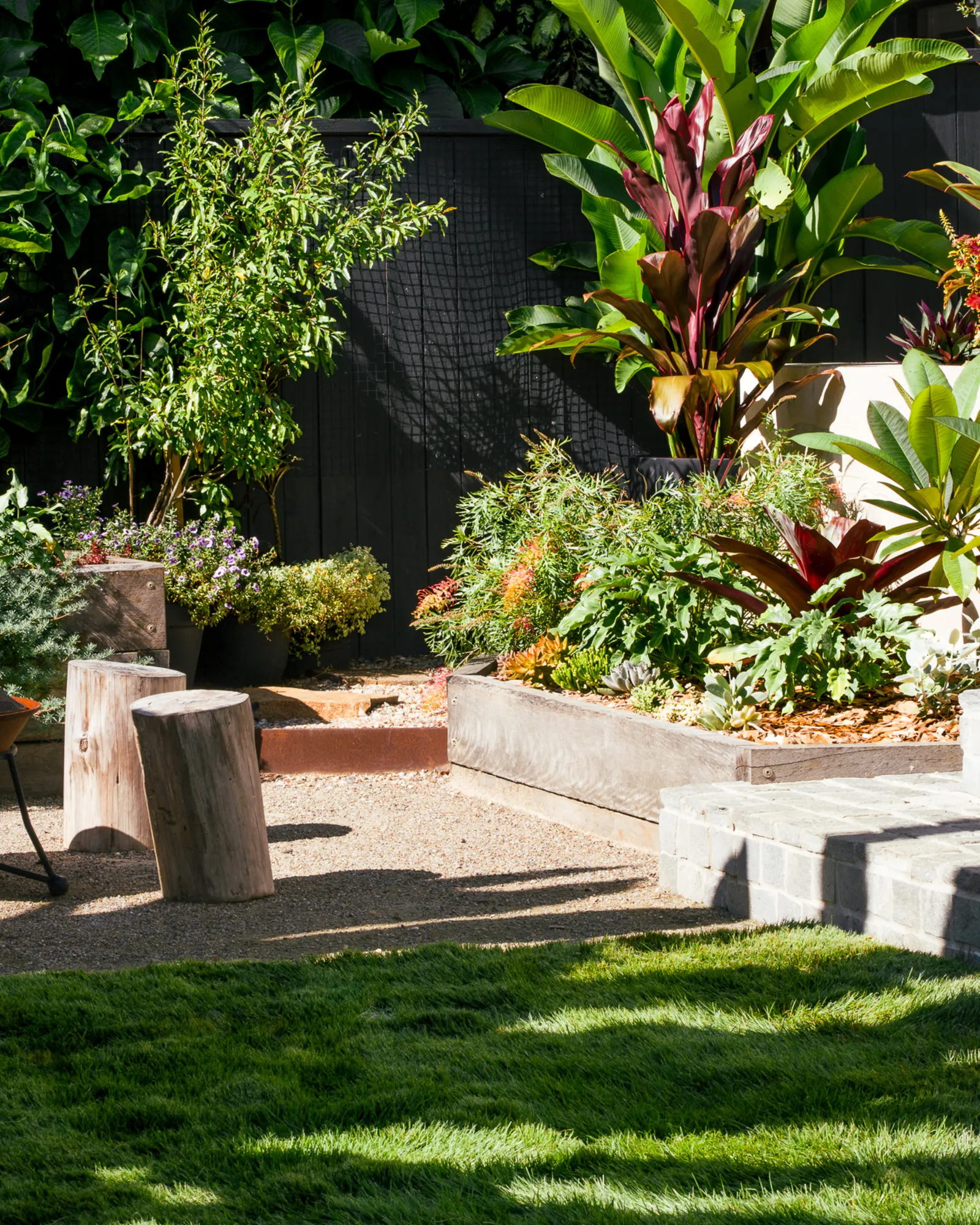 Rendered garden beds planted out beside a strip of lawn, with timber stump seats