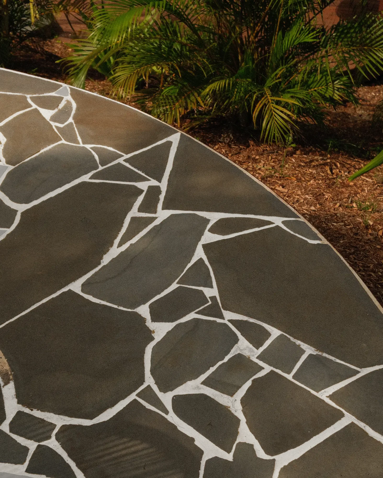 A circle of sandstone crazy paving laid into mulch and planting